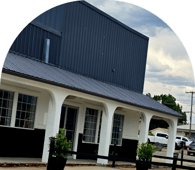 A white porch with columns and a dark blue building behind it under a cloudy sky.