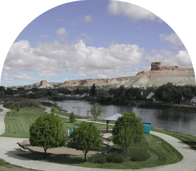 A river flowing beside a city with green trees and a partly cloudy sky.