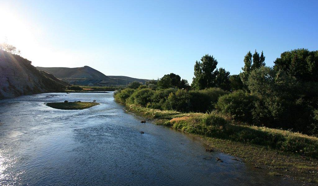 A serene river flowing through a landscape with trees and hills.